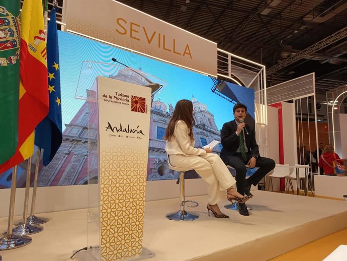 El diputado de Cultura conversa con la periodista Alejandra Cosgaya en la presentación de la oferta cultural en Fitur.