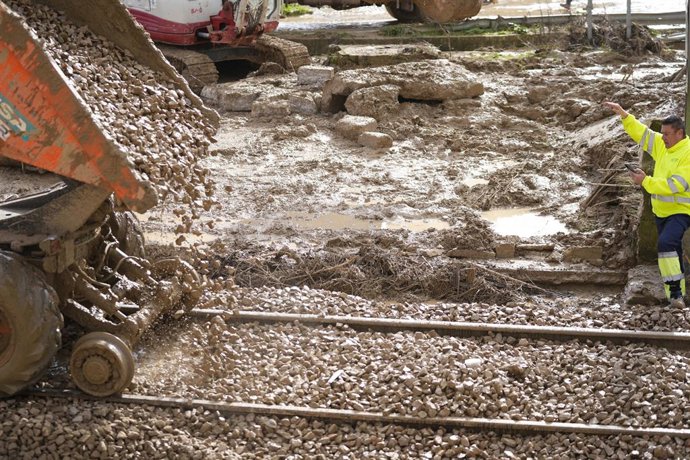 Operarios de Adif reponen grava en la vía, mientras una excavadora (al fondo) retira los restos del muro colapsado.