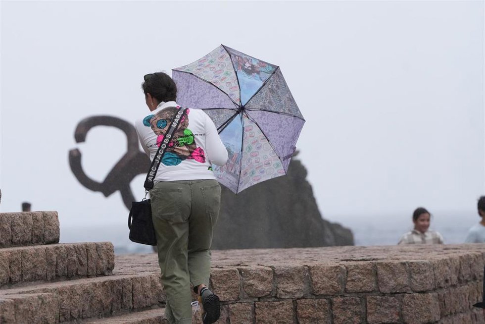 Archivo - Una mujer camina con un paraguas junto al Peine del Viento, en San Sebastián