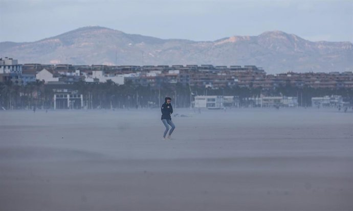 Archivo - Una mujer camina por la playa mientras le da el viento en València