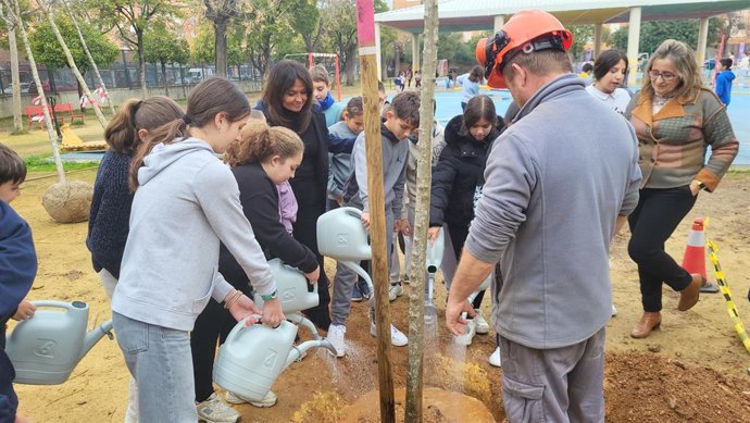 La delegada de Parques y Jardines, Evelia Rincón, junto a alumnos plantando árboles en un colegio.