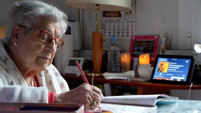 Una mujer mayor hace tareas de escritura, junto al dispositivo de voz de Cruz Roja.