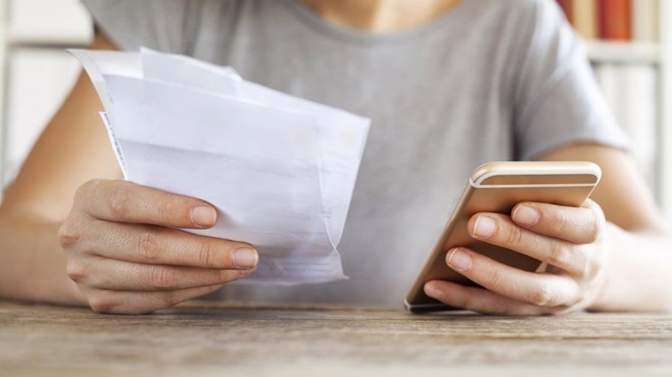 Archivo - Persona sujeta un teléfono y una factura