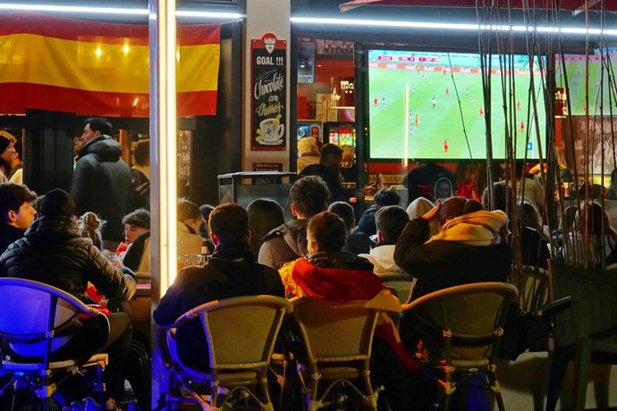 Archivo - Varios aficionados ven en la televisión de un bar un partido de fútbol 