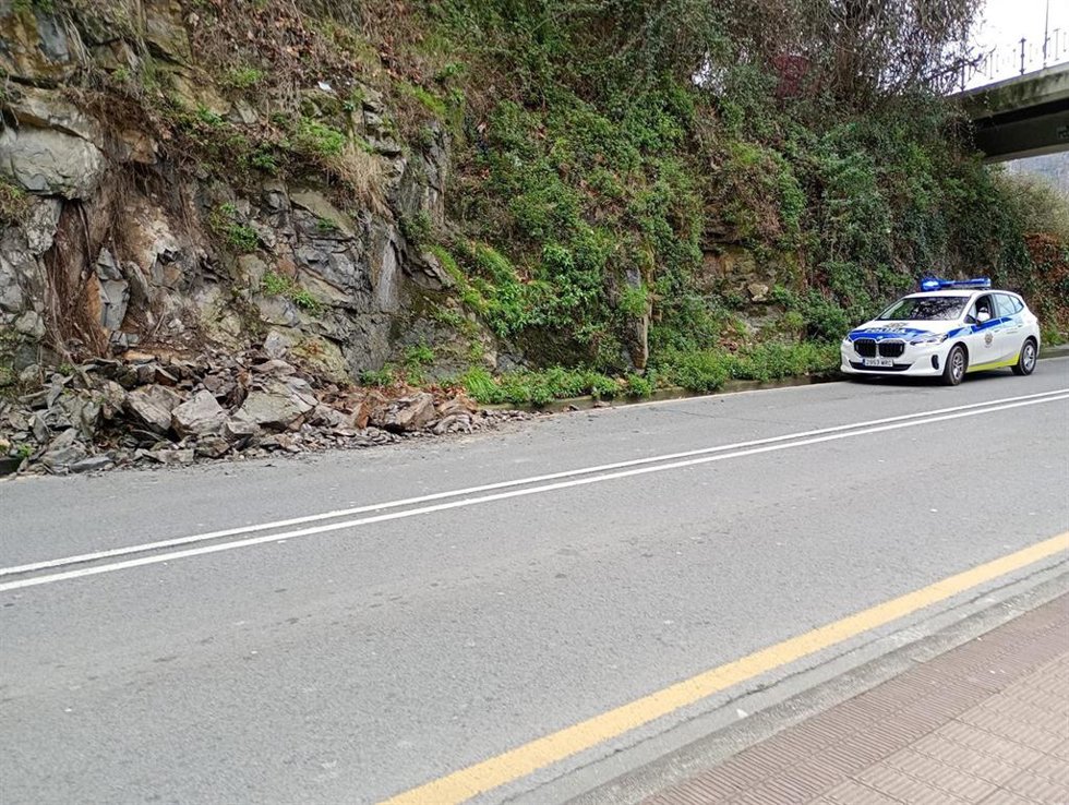 Un coche patrulla de la Policía Municipal de Barakaldo junto a la ladera donde se han desprendido piedras y tierra sobre la calzada