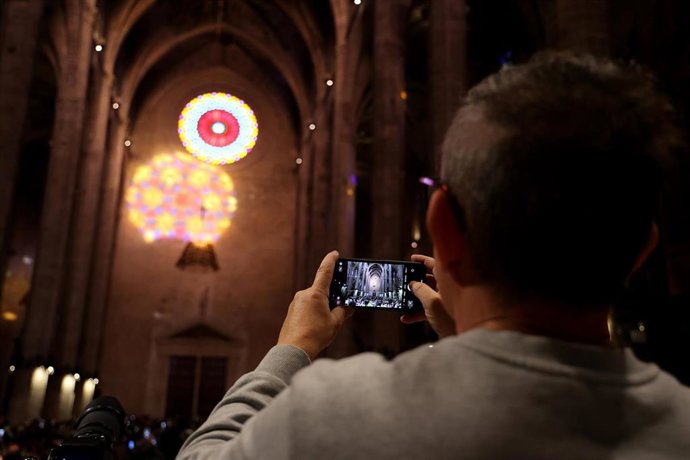 Archivo - Un hombre fotografía los colores del rosetón mayor reflejados sobre la pared, durante la ‘Festa de la llum’.