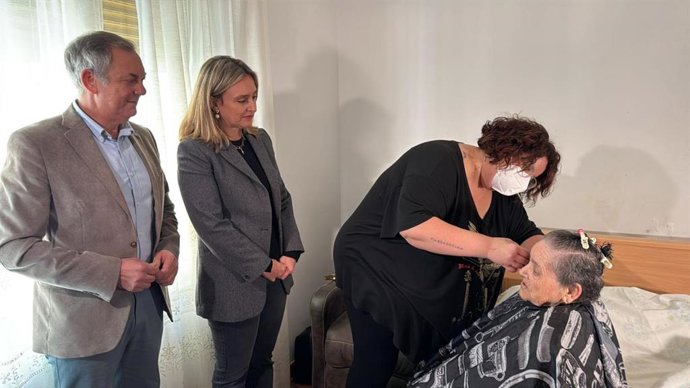 Una mujer mayor recibe servicios de peluquería en su casa, en el marco del programa 'Cercanos'