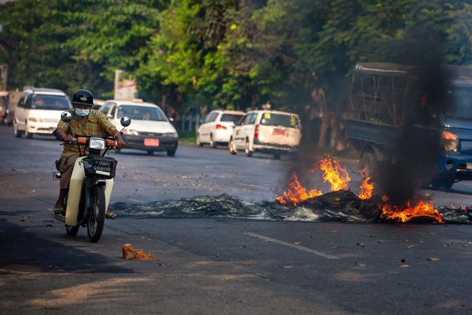 Archivo - Un hombre conduce su motocicleta junto a neumáticos en llamas durante una manifestación contra el golpe militar y la detención de líderes civiles en Yangon, Birmania.