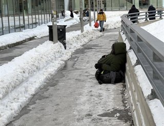 Un hombre sin hogar se sienta en el suelo rodeado de nieve frente a la terminal del ferry de Staten Island, en Nueva York