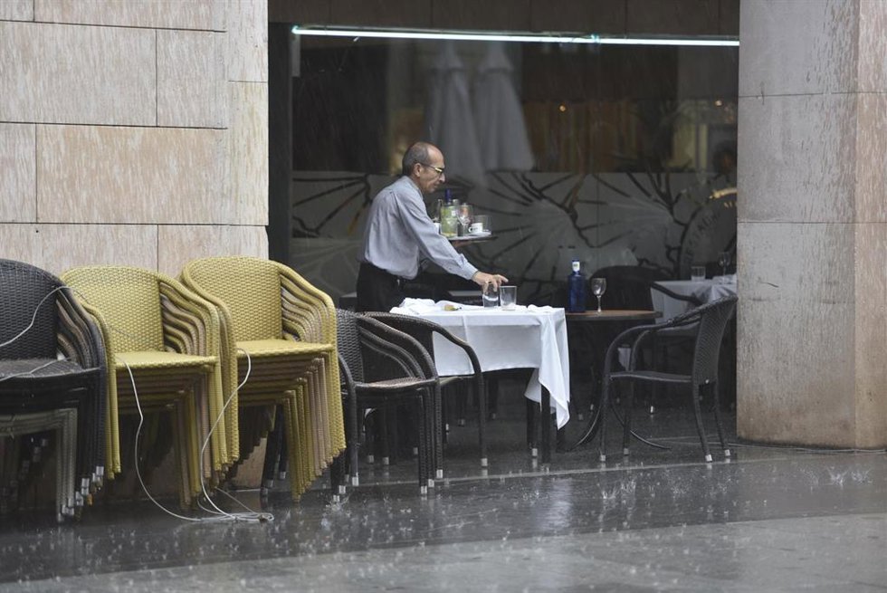 Archivo - Un camarero recoge una mesa en una terraza mientras llueve
