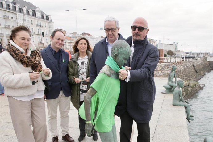 Acto del Día Mundial contra el Cáncer en Cantabria. El consejero de Salud, César Pascual (derecha), coloca un pañuelo de la AECC en una de las estatuas de Los Raqueros de Santander