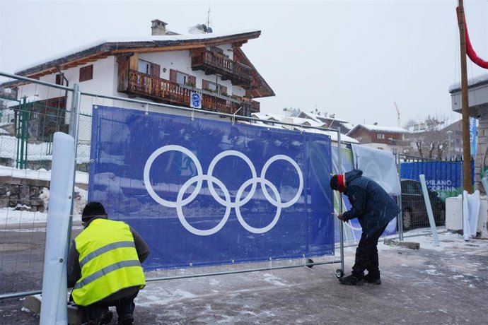 Dos trabajadores colocan un cartel con los aros olímpicos en los Juegos de Invierno de Milán-Cortina d'Ampezzo 2026.
