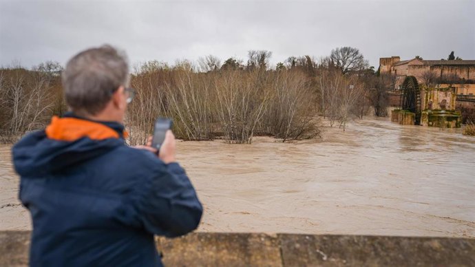 El río Guadalquivir pasa en nivel rojo este jueves por toda la provincia de Córdoba. Un viandante fotografía el caudal, en la capital