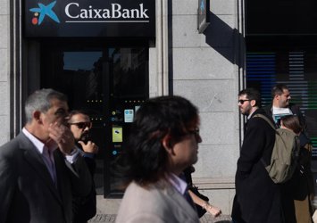 Archivo - Varias personas pasan delante de una entidad financiera CaixaBank en imagen de archivo. 