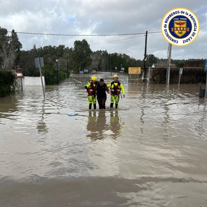 Dos bomberos ayudan a una persona en Arcos a salir de la zona inundada con motivo de la crecida del agua por la apertura de la presa.