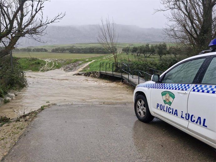 Vehículo de la Policía Local ante un arroyo con el caudal crecido en Cuevas del Becerro durante la borrasca Leonardo a 4 de febrero de 2026