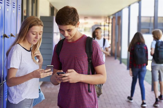 Archivo - Two friends talking and using phones in school corridor.