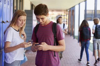Archivo - Two friends talking and using phones in school corridor.