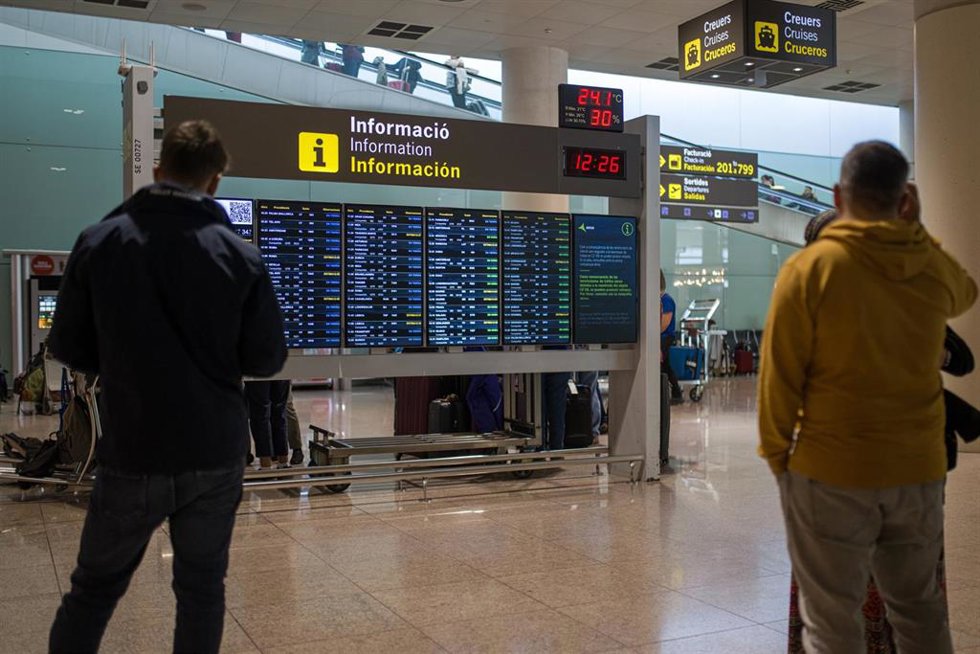 Archivo - Varias personas observan un panel de llegadas en el aeropuerto de Barcelona, en una imagen de archivo