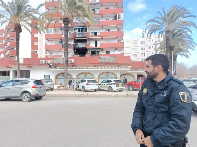 L'agent 64 de la Policia Local de Xàbia junt amb l'edifici de l'habitatge incendiat