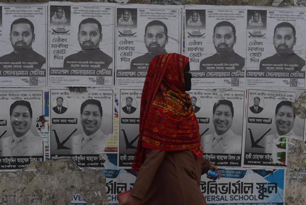 Archivo - Una mujer delante de varios carteles durante la campaña electoral para las elecciones en Bangladesh.