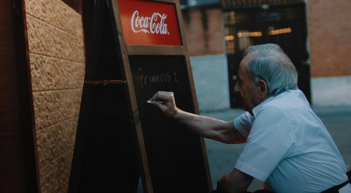 Camarero escribiendo menú en pizarra de Coca-Cola.