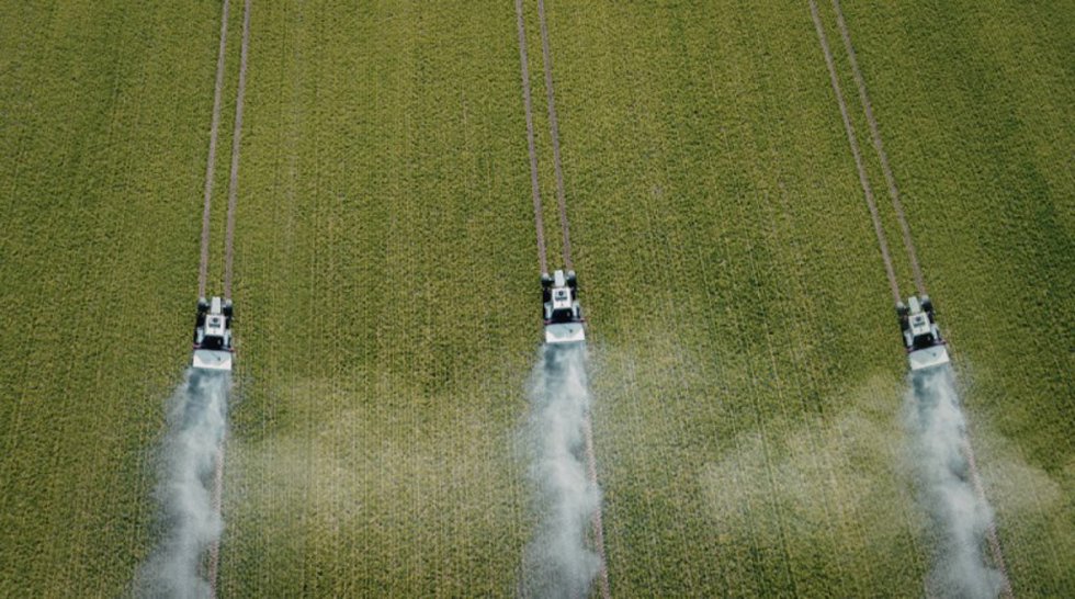 Imagen de recurso de vehículos agrículos en pleno trabajo sobre un cultivo.