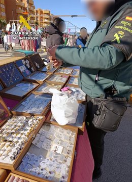 Un agente de la Patrulla de Fiscal y Fronteras de la Guardia Civil inspecciona piezas expuestas en un puesto de venta ambulante del mercadillo de Puerto de Mazarrón, en Mazarrón (Murcia)