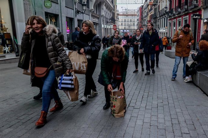 Archivo - Varias personas caminan con bolsas de las rebajas en la calle Preciados, en Madrid (España).