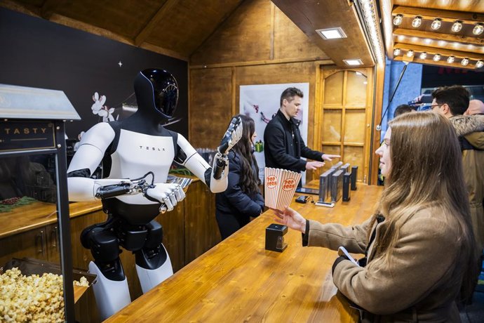 Archivo - 20 December 2025, Berlin: Tesla's humanoid robot 'Optimus' hands out popcorn to Lisa (R) during its presentation at the Mall of Berlin. Photo: Christoph Soeder/dpa