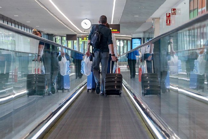 Archivo - Un hombre lleva una maleta de cabina en la cinta de un aeropuerto.