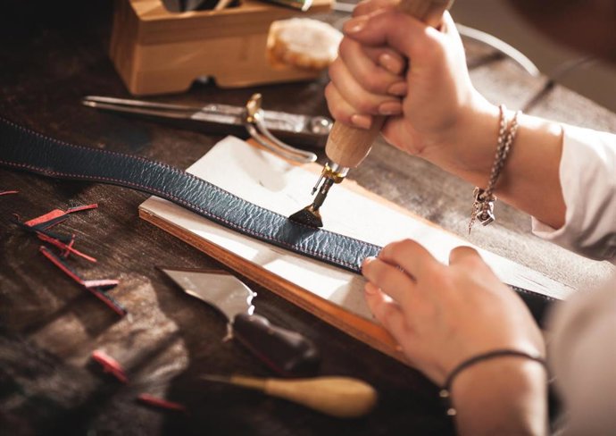 Archivo - Un artesano confecciona un cinturón de cuero.