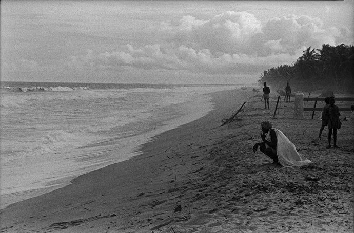 Archivo - November 19, 2025, Cologne, North Rhine-Westphalia, Ghana: man crouches on the beach near the surf, other people stand at a distance along the palm-fringed coast, 1963. Ghana, 1960s, 11.07.1963.