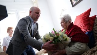 El presidente de la Diputación de Almería, José Antonio García Alcaina, entrega un ramo de flores a Carmen Amate durante la visita realizada a su domicilio en Alhama de Almería.