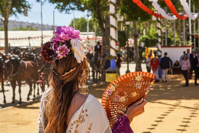 Archivo - Una mujer vestida de flamenca se abanica en el recinto ferial de la Feria de Abril de Sevilla, en foto de archivo.