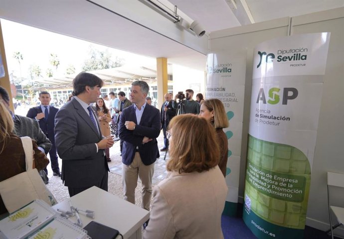 Rodríguez Hans, al fondo, conversa con el rector de la UPO en el stand de Prodetur en la Feria del Empleo y el Emprendimiento, que se celebra en el campus universitario.