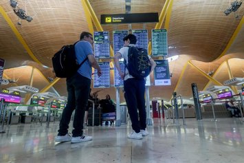 Archivo - Dos personas observan el panel de salidas con motivo de la operación salida del puente de agosto, en la T4, en el aeropuerto Adolfo Suárez Madrid-Barajas, a 14 de agosto de 2024, en Madrid (España).  