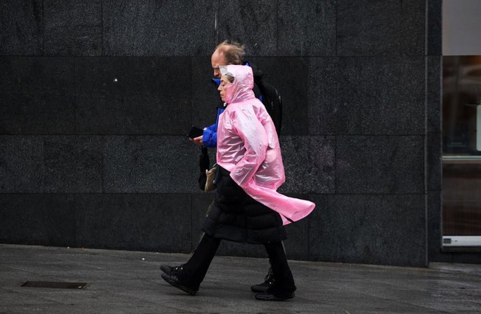 Archivo - Imagen de archivo de transeúntes por el centro de Málaga protegiéndose de la lluvia y el fuerte viento.