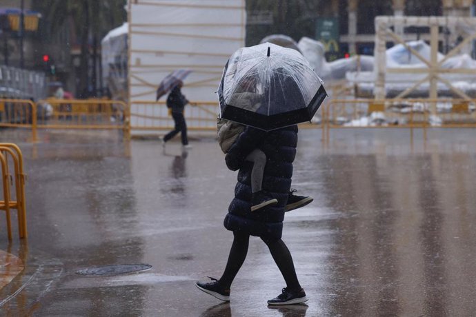Personas caminan ante ninots tapados con plásticos por la lluvia durante el montaje de las Fallas 2026, en la plaza del Ayuntamiento, a 5 de marzo de 2026, en Valencia, Comunidad Valenciana (España).