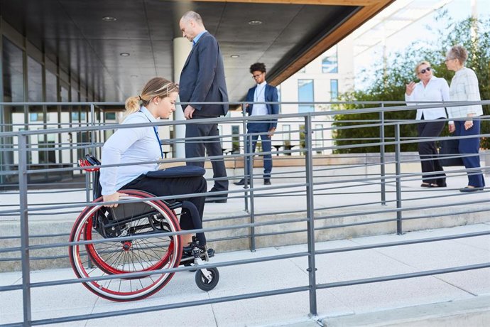 Archivo - Una mujer en silla de ruedas accede por una rampa a un edificio municipal en foto de archivo.