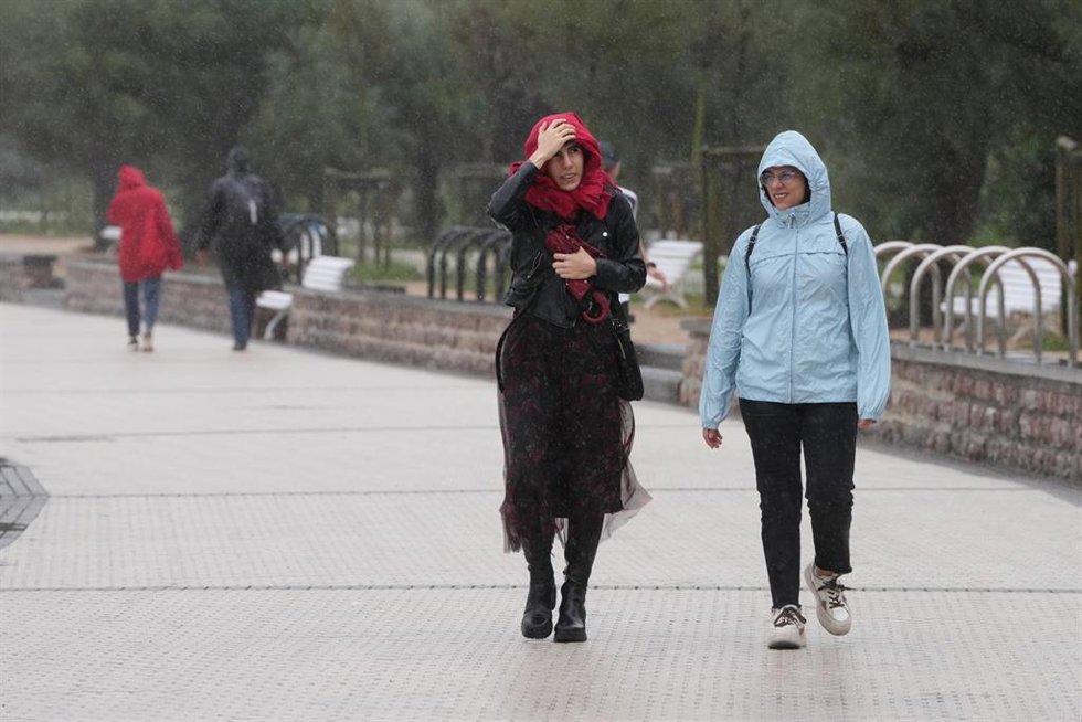Archivo - Dos personas caminan bajo la lluvia en la playa de Ondarreta
