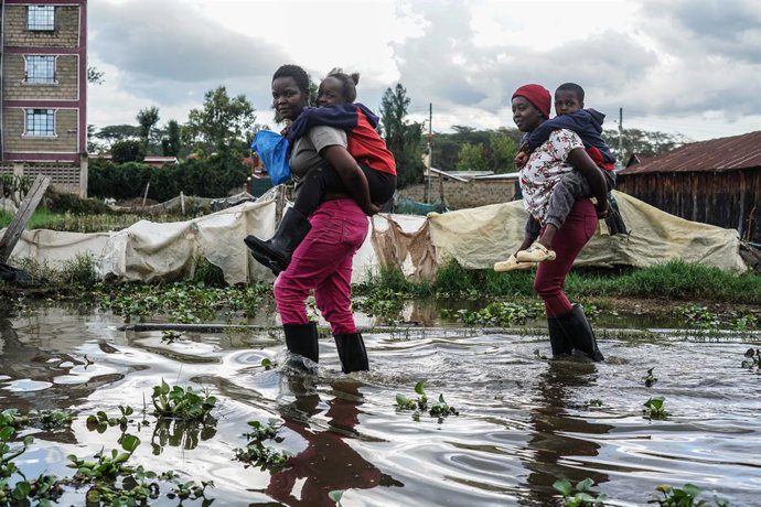 Archivo - November 8, 2025, Naivasha, Kenya: Women carry children on their backs as they wade through a flooded street in Kihoto, a low income village severely affected by the rising waters of nearby Lake Naivasha. Hundreds of people have continued to eva
