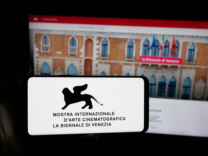 Archivo - Una persona sostiene un teléfono con el logotipo del la Bienal de Venecia frente al sitio web.