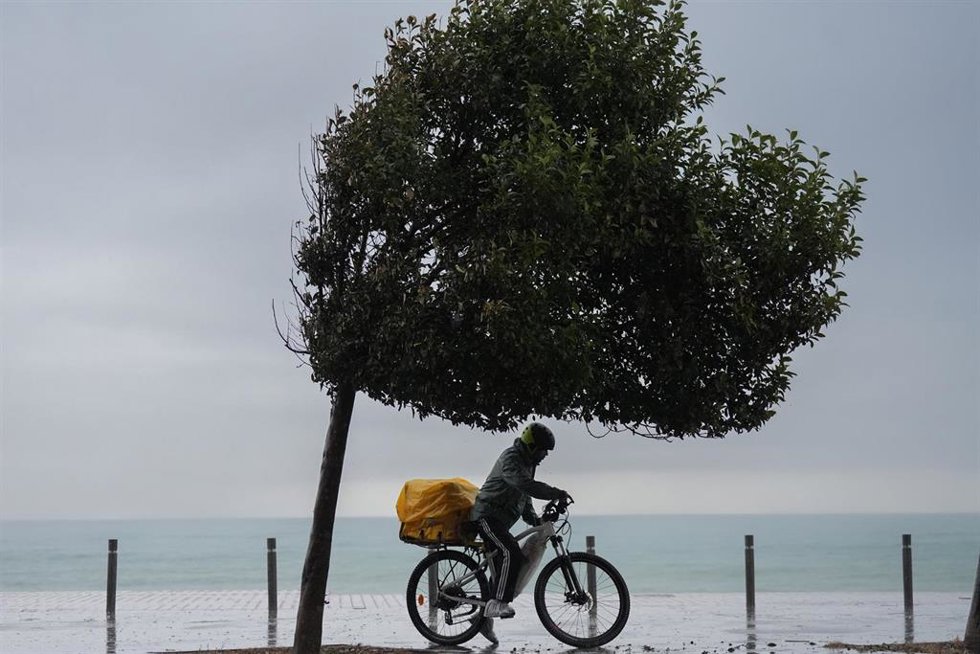 Archivo - Dos hombres en bicicleta bajo la lluvia en una playa.