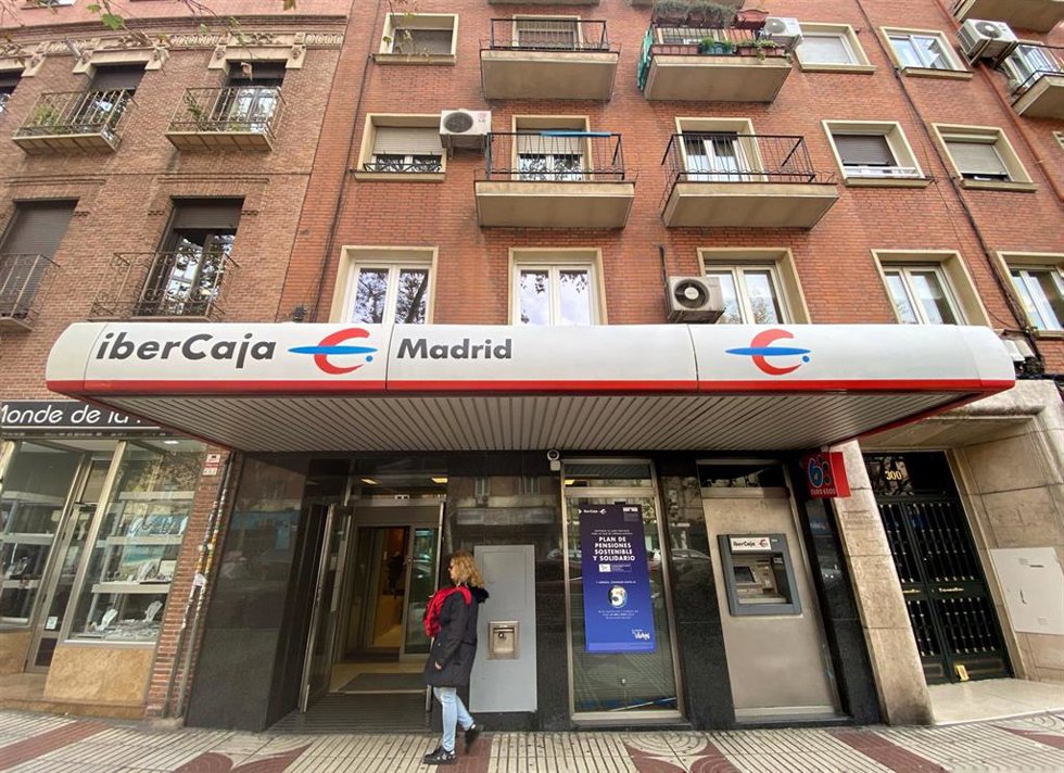 Archivo - Una mujer entra en un una oficina de IberCaja en Madrid.