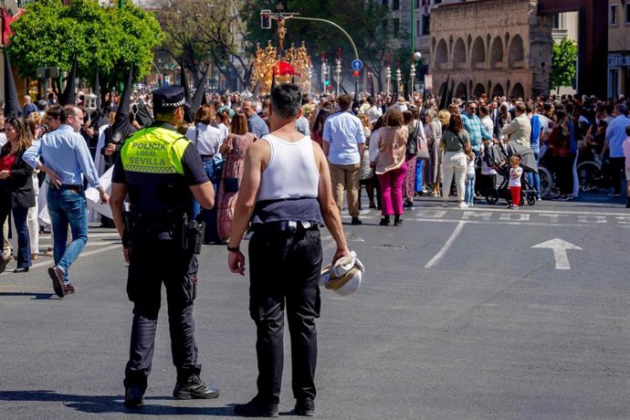 Archivo - Un policía municipal y un costalero viendo el cortejo de  la Hermandad de la Sed por a Av Luis Montoto en una imagen de archivo.