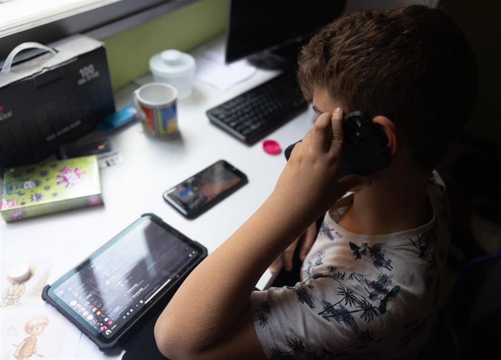 Archivo - Un niño usa un teléfono móvil y una tableta