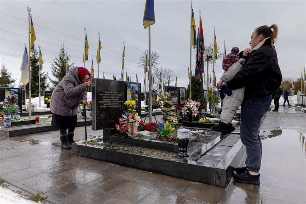 Una mujer anciana reza en Bucha ante la tumba de un ser querido que murió en la guerra, en el cuarto aniversario del ataque de Rusia contra Ucrania.
