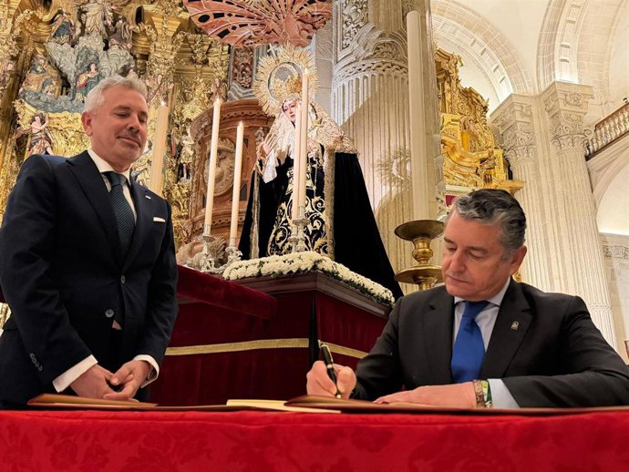 El consejero Antonio Sanz firma en el libro de honor de la Hermandad del Amor en presencia de su hermano mayor, en la Iglesia del Salvador.