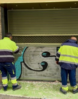 Operarios de limpieza del Ayuntamiento de Huesca eliminan un grafiti de una persiana comercial.